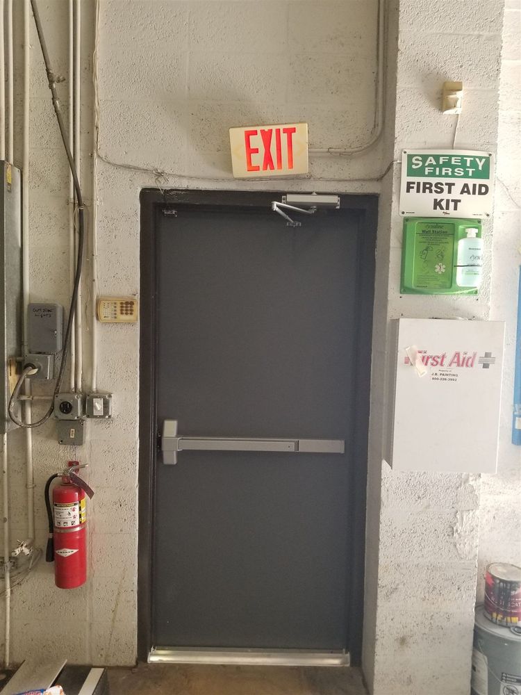 Steel exit door with panic bar beside a first aid kit and extinguisher