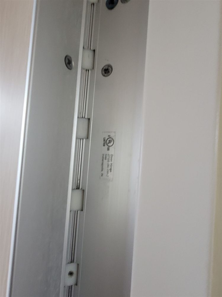 Close-up of a labeled continuous hinge fastened along the hinge edge of a commercial door