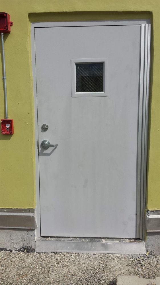 Gray hollow metal door on a yellow stucco wall with a full-height continuous hinge