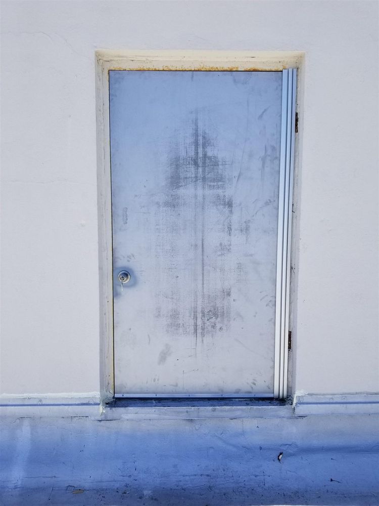 Weathered gray steel rooftop door fitted with a new continuous hinge over the old butt-hinge frame